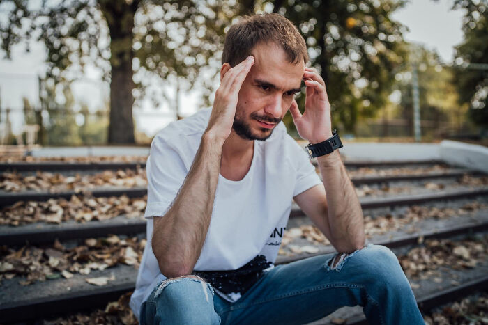 Young man sitting outdoors looking stressed, illustrating small signs of a difficult childhood experience.