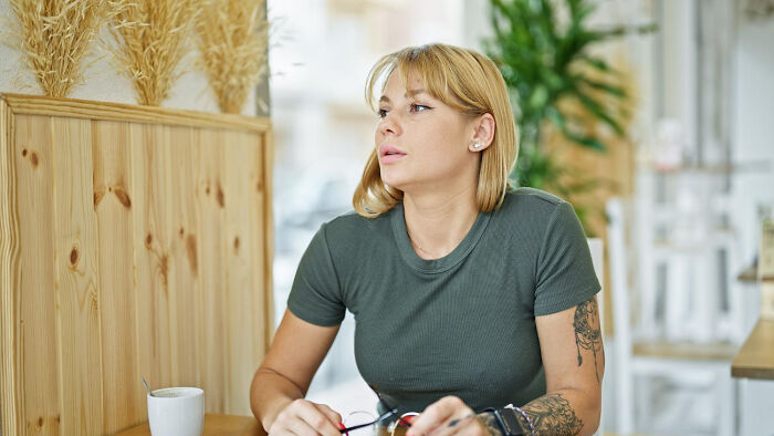 Young woman with tattoos sitting thoughtfully in a cafe, reflecting on the deepest secrets parents kept from their kids.