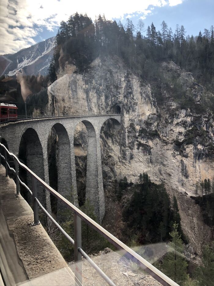 Scenic travel photo of a stone arch bridge crossing a deep gorge surrounded by forested mountains.
