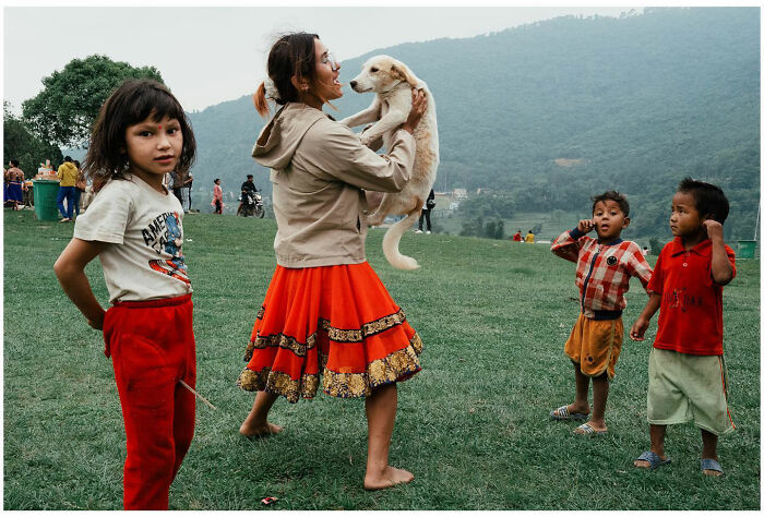 Children and a woman holding a puppy in a grassy outdoor area, capturing raw and captivating street moments in Asia.