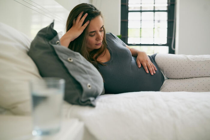 Pregnant woman resting on a bed, holding her belly and reflecting on pregnancy, childbirth, and postpartum facts.