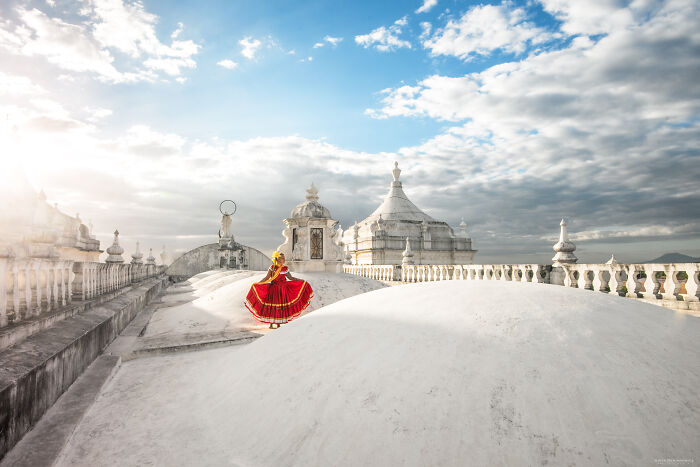Woman in a vibrant red dress on a historic white rooftop under a bright sky in breathtaking travel photos.
