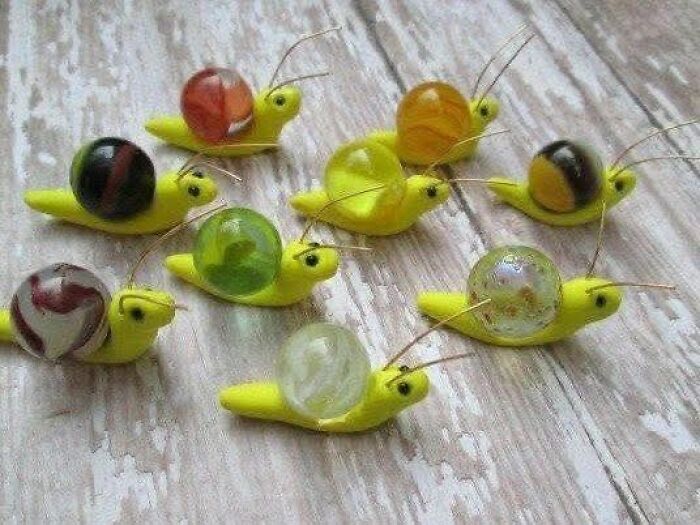 Funny craft shaming example with DIY snail figurines made from marbles and yellow clay on a wooden surface.