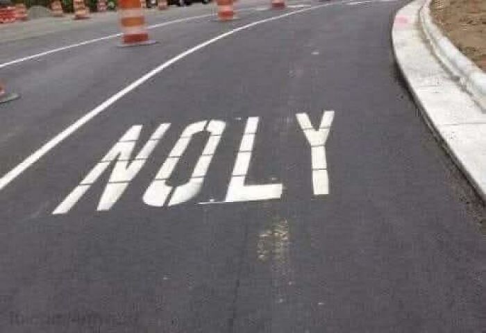 Road under construction with orange barrels and a misspelled work sign showing funny work meme humor.