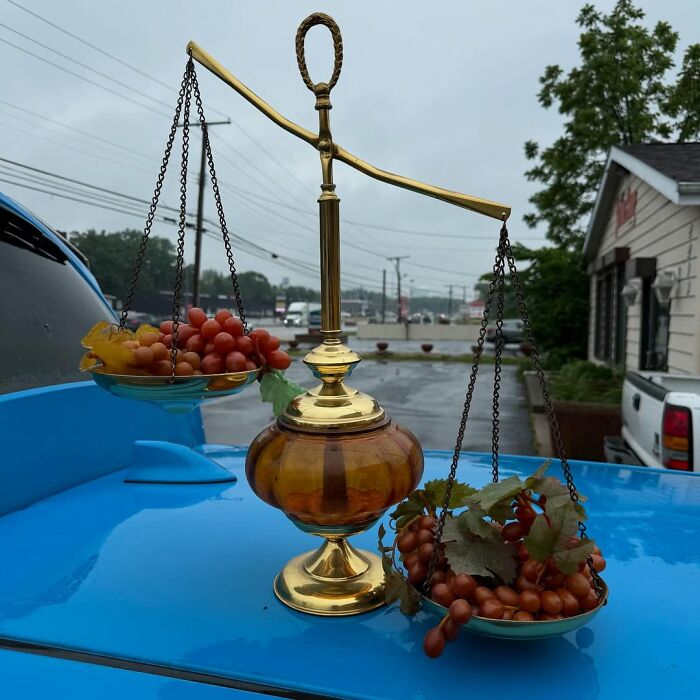 Antique brass balance scale with artificial grapes on each side, showcasing cool secondhand finds outdoors on a blue surface.