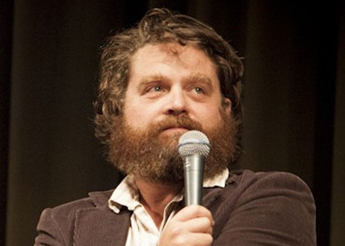 Bearded man holding a microphone, representing celebrities before fame in a casual speaking or performance setting.