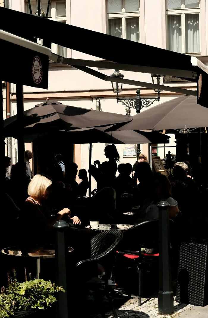 Street shots of people sitting and interacting under umbrellas at an outdoor cafe, capturing the poetry of everyday life.