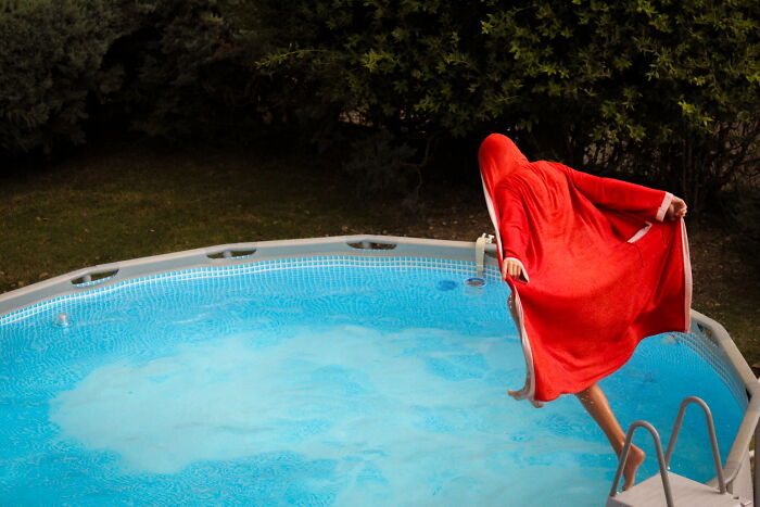 Person in a red cloak captured mid-air jumping into a pool, showcasing a perfectly-timed street photo by Luca Regoli.