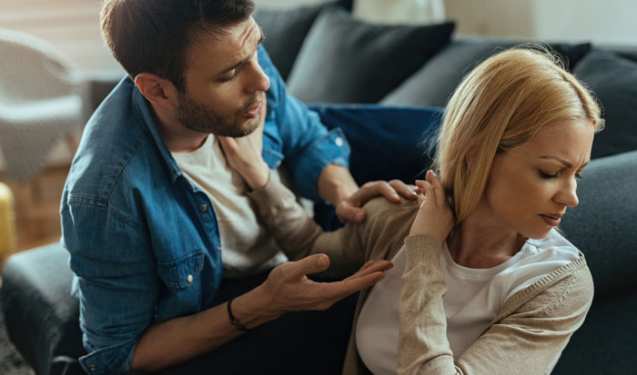 Man in distress expressing regret and sadness while woman turns away upset in a tense relationship moment at home.