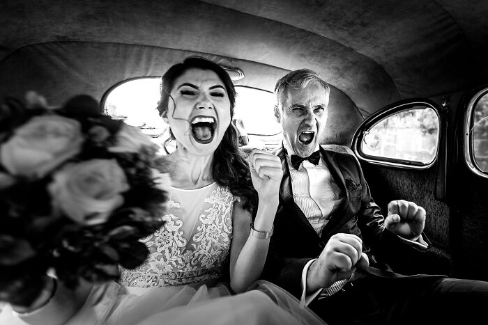 Bride and groom celebrating joyfully inside a vintage car, captured in one of the unforgettable wedding photos.