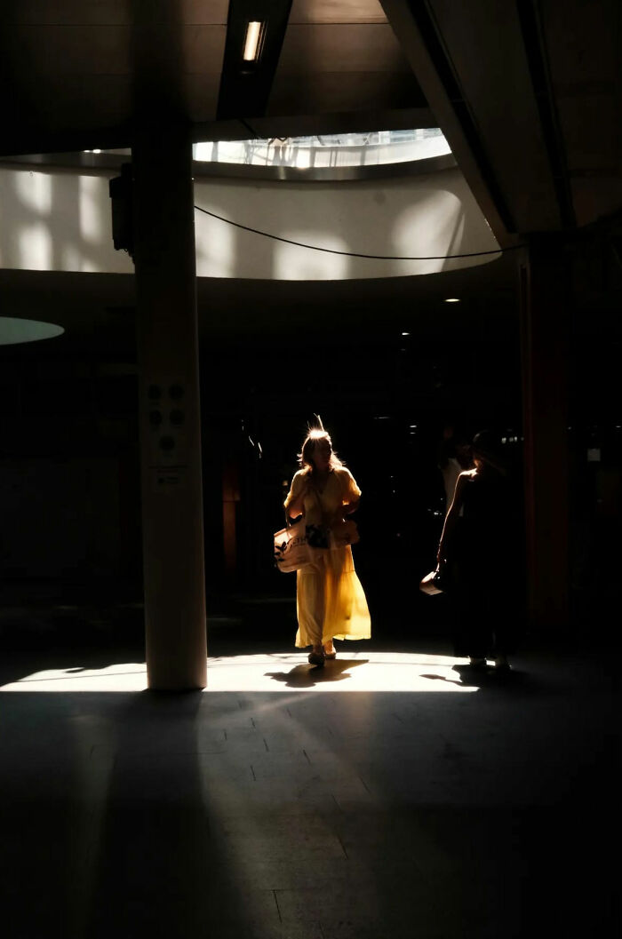 Woman in yellow dress walking through dramatic light in a street shot capturing the poetry of everyday life.