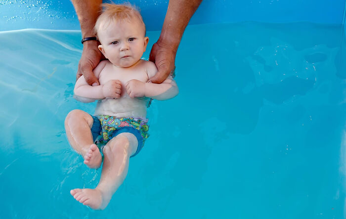 Baby learning to swim in a pool with adult support, illustrating unusual things people really did in public.