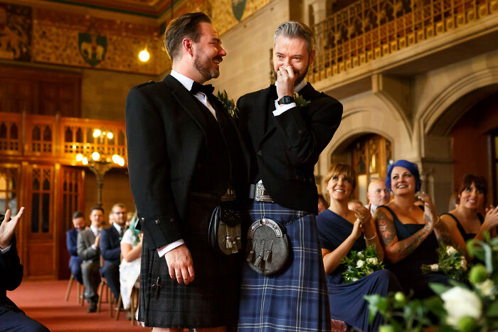 Two grooms in kilts sharing a joyful moment during an unforgettable wedding ceremony with guests applauding.