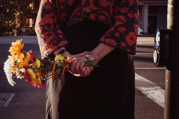 Person holding colorful bouquet of flowers candidly on a city street in a warm light street photo by Alex McClintock