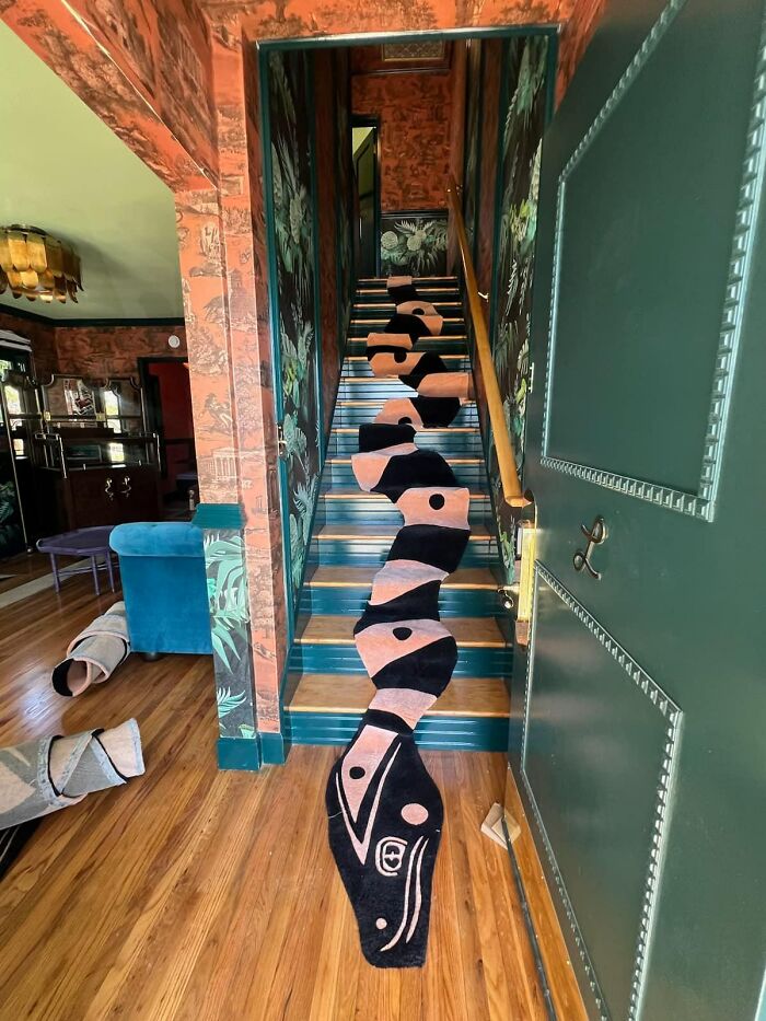 A snake-shaped rug stretches dangerously along narrow indoor stairs, creating a hazardous death stairs effect in a decorated home.