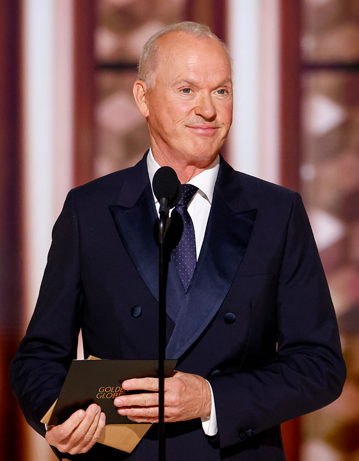 Male celebrity in a black tuxedo speaking at an event, illustrating celebrities who look way younger than they actually are.