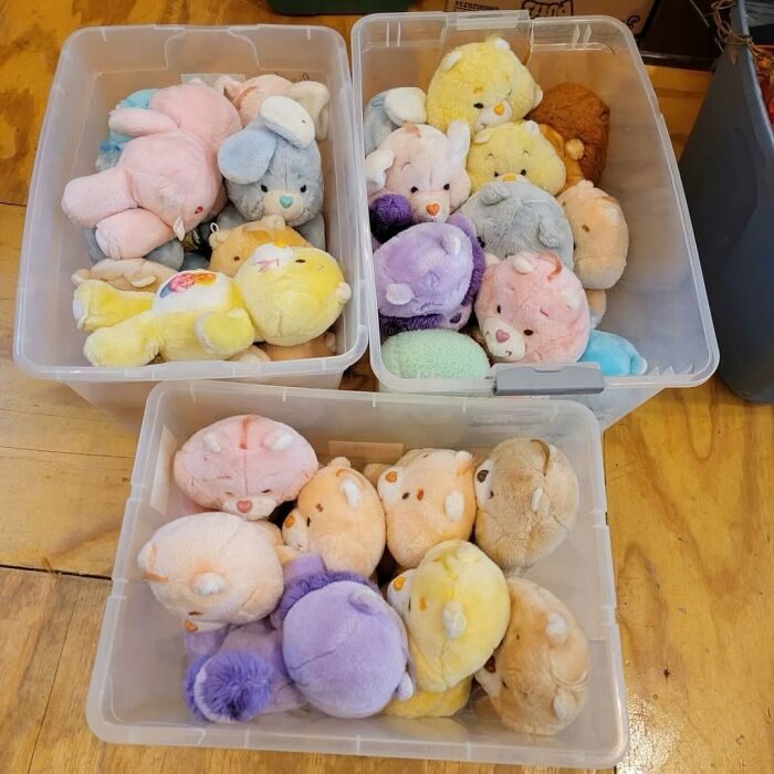 Three plastic bins filled with colorful secondhand plush toys resting on a wooden floor as cool secondhand finds.