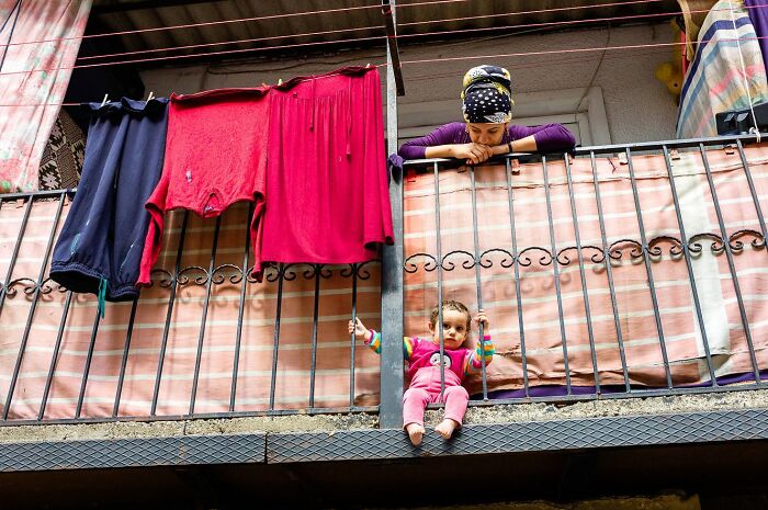 Child and woman on balcony with colorful clothes hanging, captured by street photographer in a candid urban moment.