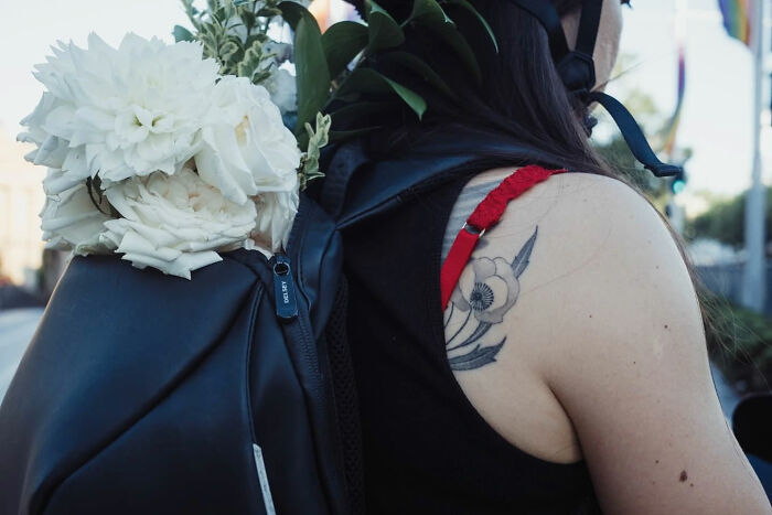 Woman with floral tattoo on shoulder carrying black backpack with white flowers in candid street photo by Alex McClintock