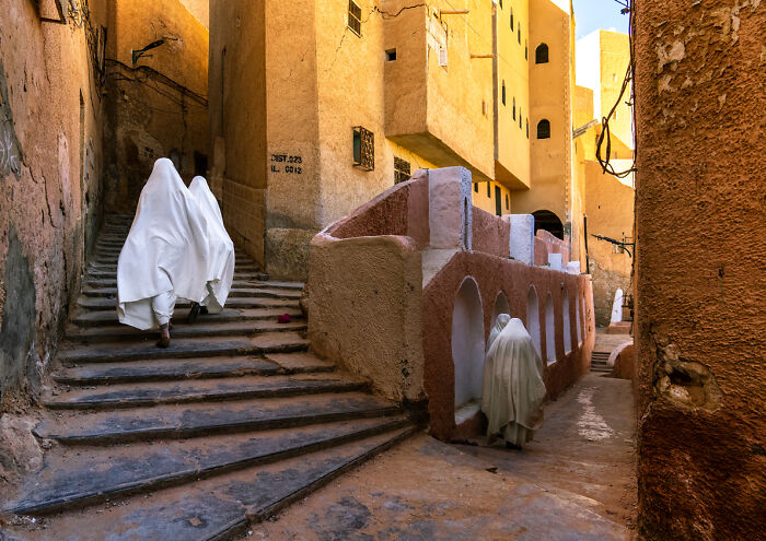 Traditional clothing worn by travelers walking up stone steps in a sunlit narrow alley, breathtaking travel photos scene