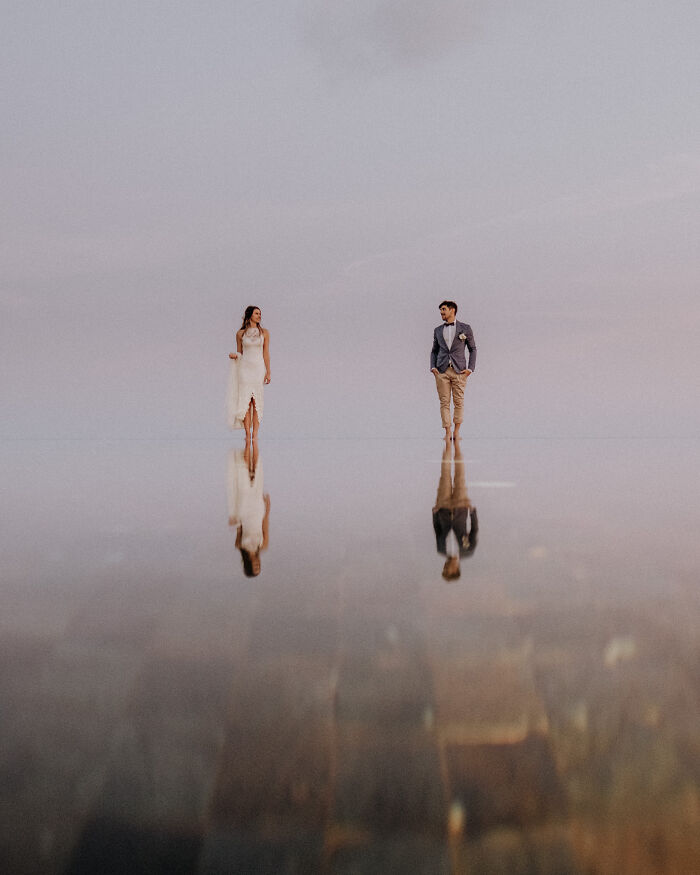 Bride and groom walking barefoot on reflective surface, creating a stunning unforgettable wedding photo with soft pastel sky.
