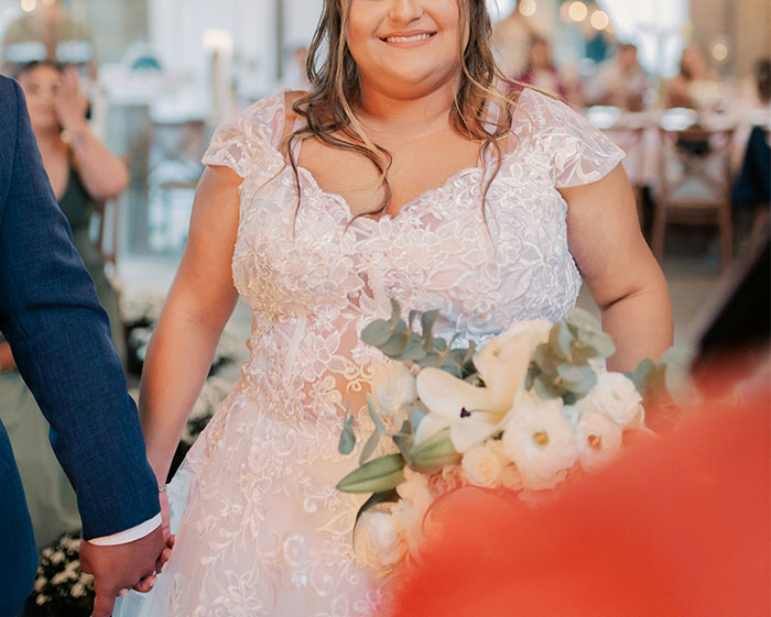 Groom&rsquo;s mom in a wedding dress with sleeves holding a bouquet, standing next to the groom at a wedding ceremony.