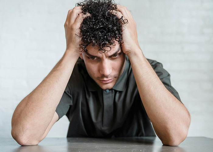 Young man with curly hair looking distressed, holding his head in hands, reflecting on a cheating wife and mind control excuse.