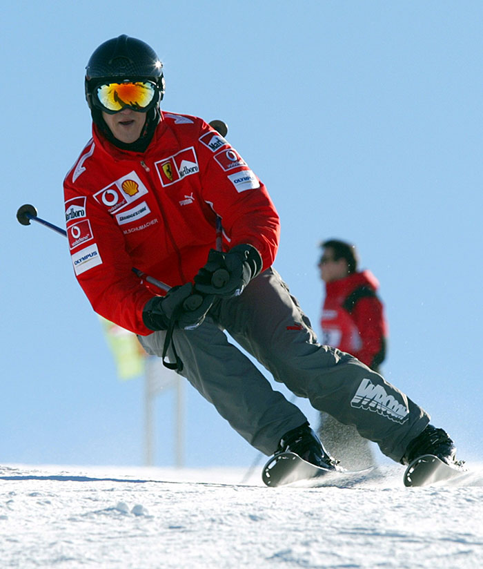 Michael Schumacher skiing in a red jacket with helmet and goggles, captured in action on a snowy slope.