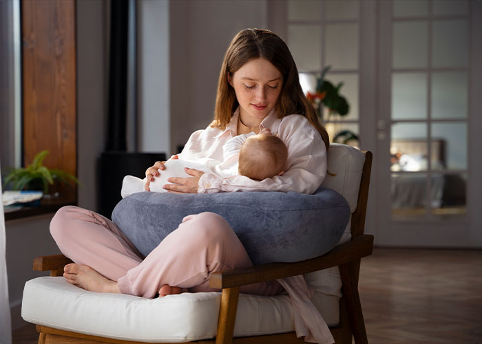 Young mother sitting in a cozy chair feeding her baby, illustrating a comforting scene linked to creepy facts that stick in your brain.