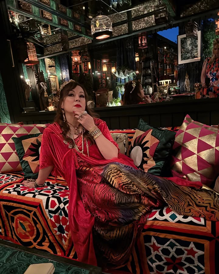 Jennifer Tilly dressed elegantly, lounging in a richly decorated room showcasing her net worth and style.