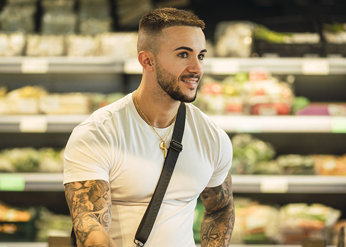 Young man with tattoos and a white shirt smiling in a grocery store, related to unhinged things men say about looks in public.