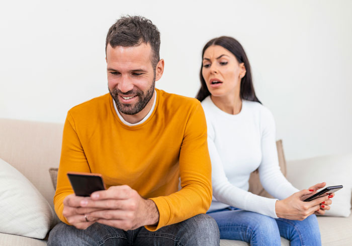 Man smiling at phone while woman looks concerned sitting together, illustrating toxic dating trends people accept as normal.