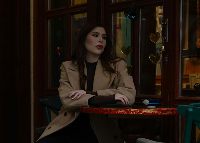 Woman in a beige coat sitting alone at a restaurant table, looking away during an awkward and painful date moment.