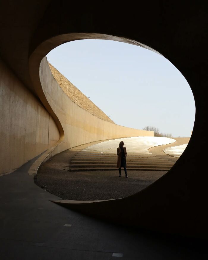 Person standing in an architectural space with curved walls, a perfect example of beautiful street shots capturing everyday life.