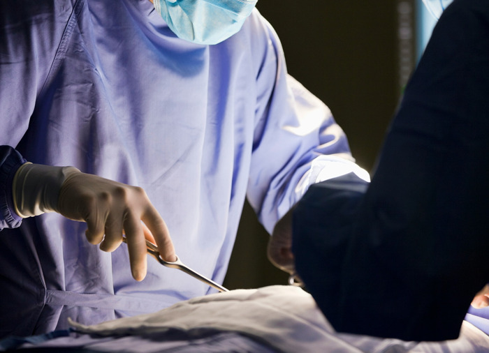 Surgeon in protective gear performing surgery while explaining how I paid for college secrets during medical training.