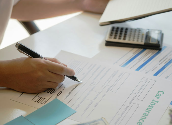 Person filling out car insurance forms at a desk with a pen and calculator, highlighting lies millennials were told growing up