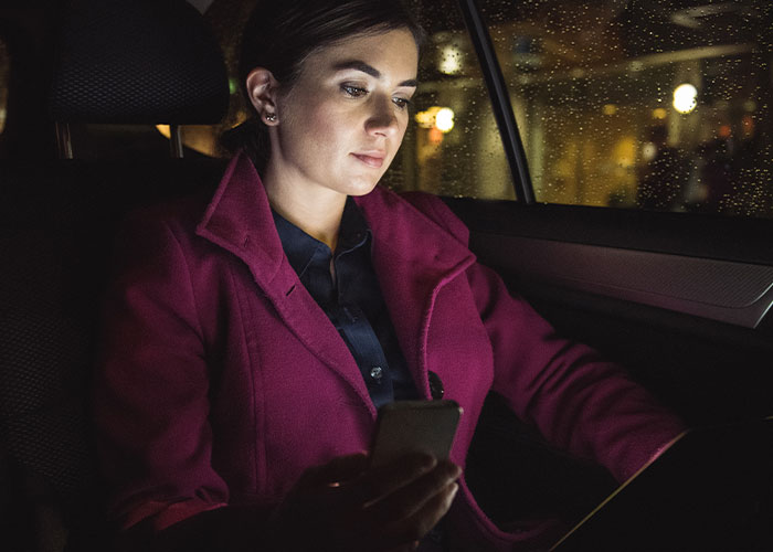Woman in a magenta coat holding a phone and focusing on safe driving facts inside a car at night in rainy weather.