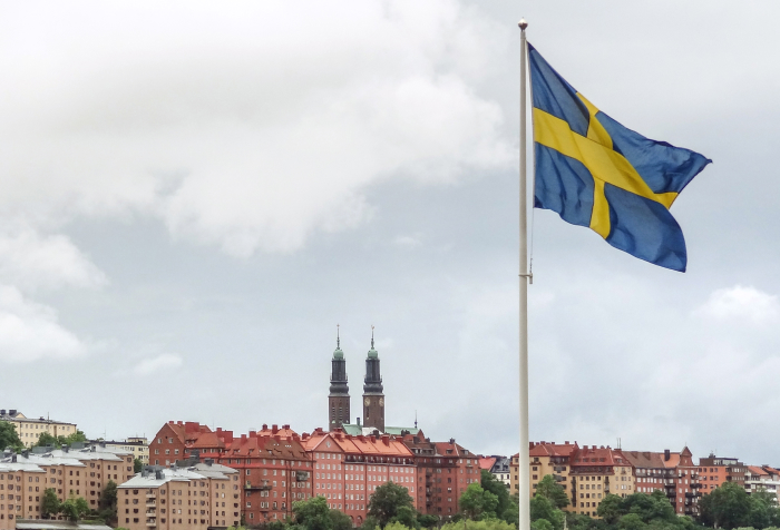 Swedish flag waving over historic cityscape under cloudy sky representing best countries to live in 2025 rankings