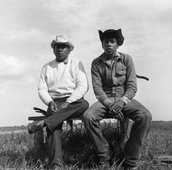 Two men wearing cowboy hats sitting outdoors in vintage cowboy photograph capturing life in the old West.