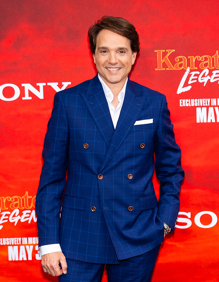Man in a blue suit smiling at a red carpet event, exemplifying celebrities who look way younger than they actually are.