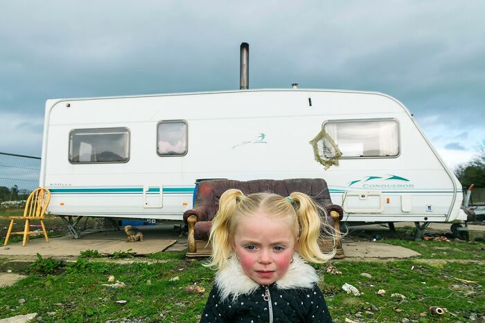 Young girl with blonde pigtails in front of a caravan, illustrating life on the margins of modern Ireland.