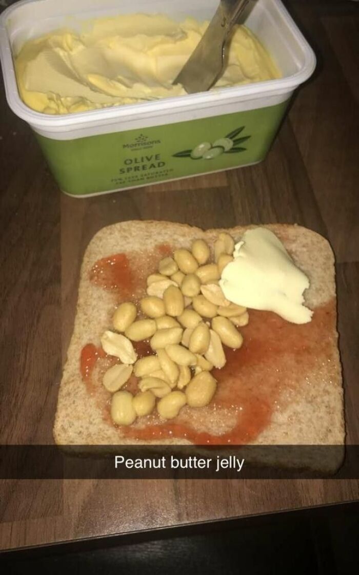 Slice of bread with jelly, shelled peanuts, and a dollop of butter next to a tub of olive spread, cursed food picture.