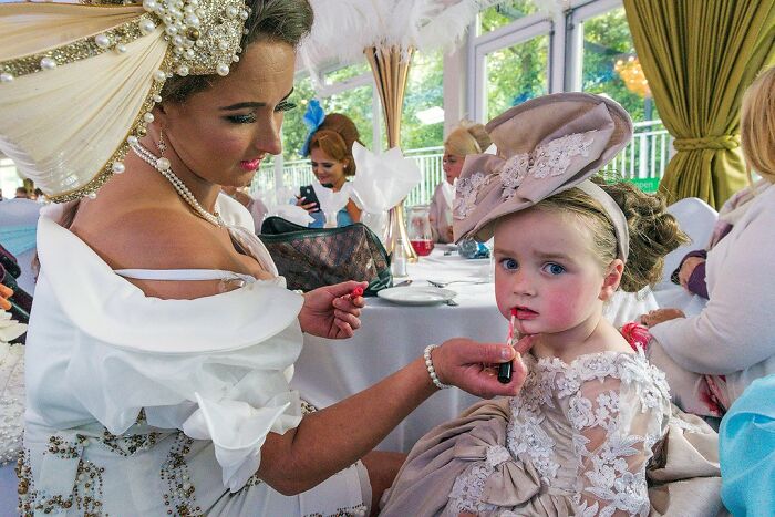 Woman applying lipstick to a young girl at a formal event, capturing life on the margins of modern Ireland.