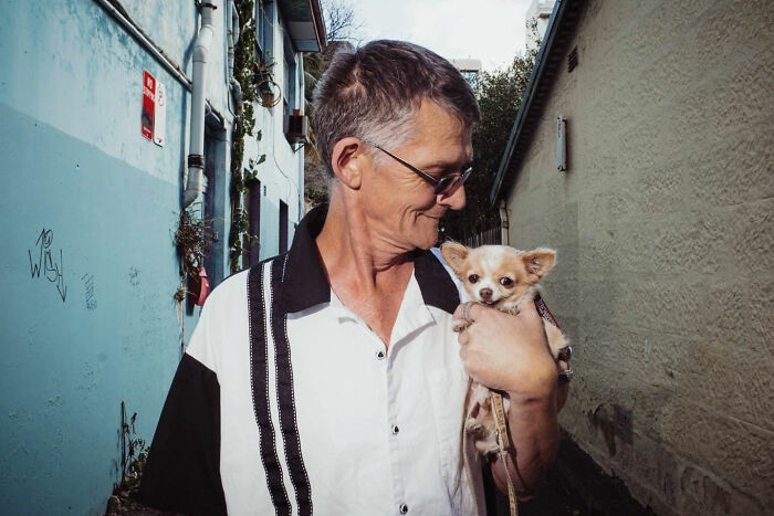 Man smiling at small dog in an alleyway, a candid street photo capturing an intimate moment by Alex McClintock.