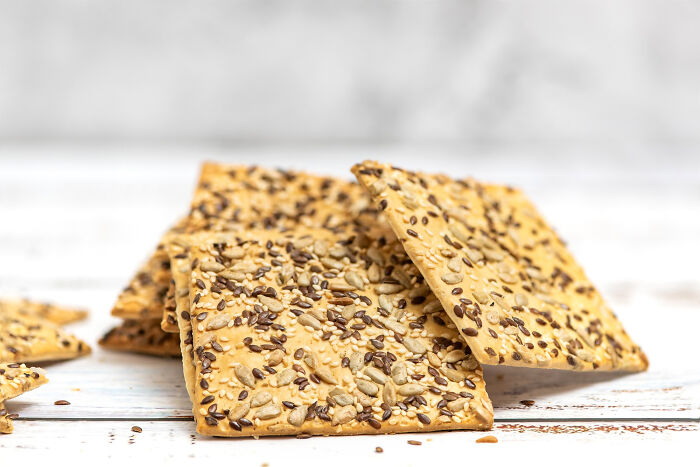Crispy seed crackers stacked on a white wooden surface, illustrating best processed foods for weight loss.