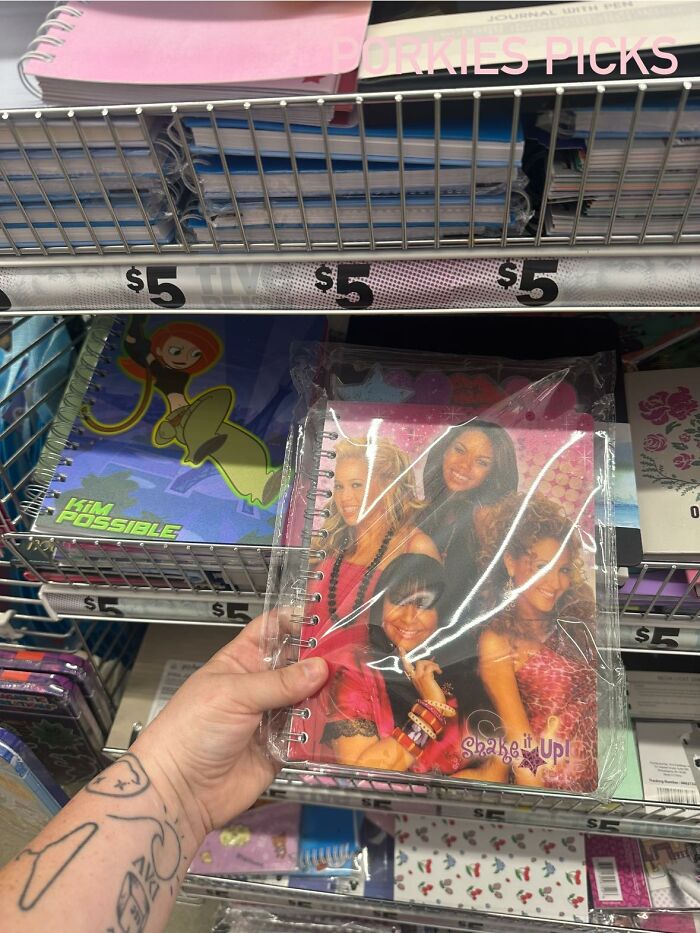 Hand holding a Shake It Up spiral notebook on a store shelf with various $5 notebooks for people who don’t fully relate to Millennials or Gen Z.