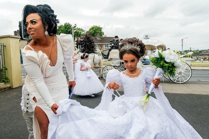 Woman helping a young girl dressed in elaborate white dress during a wedding in modern Ireland on the margins of society.