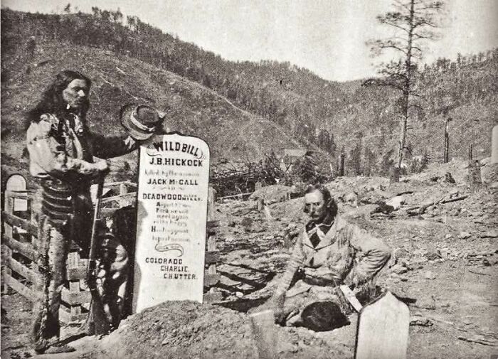 Grayscale historical photo showing two men beside a grave in a rural mountainous setting, illustrating fascinating historical moments.