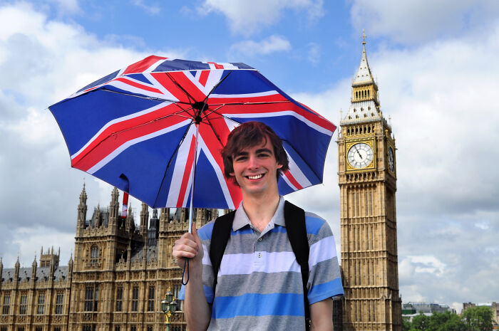 Young man holding a UK flag umbrella smiling near Big Ben, illustrating diverse opinions about the UK beyond stereotypes.