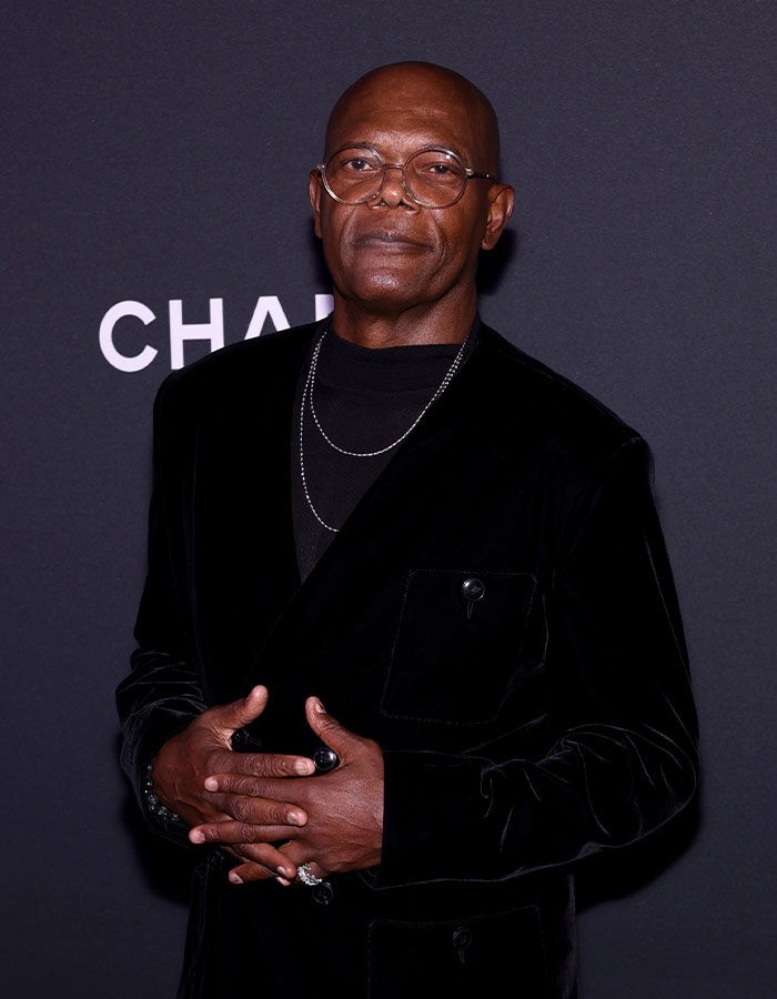 Actor wearing glasses and a black velvet jacket posing confidently, showcasing celebrities who look way younger than they actually are.
